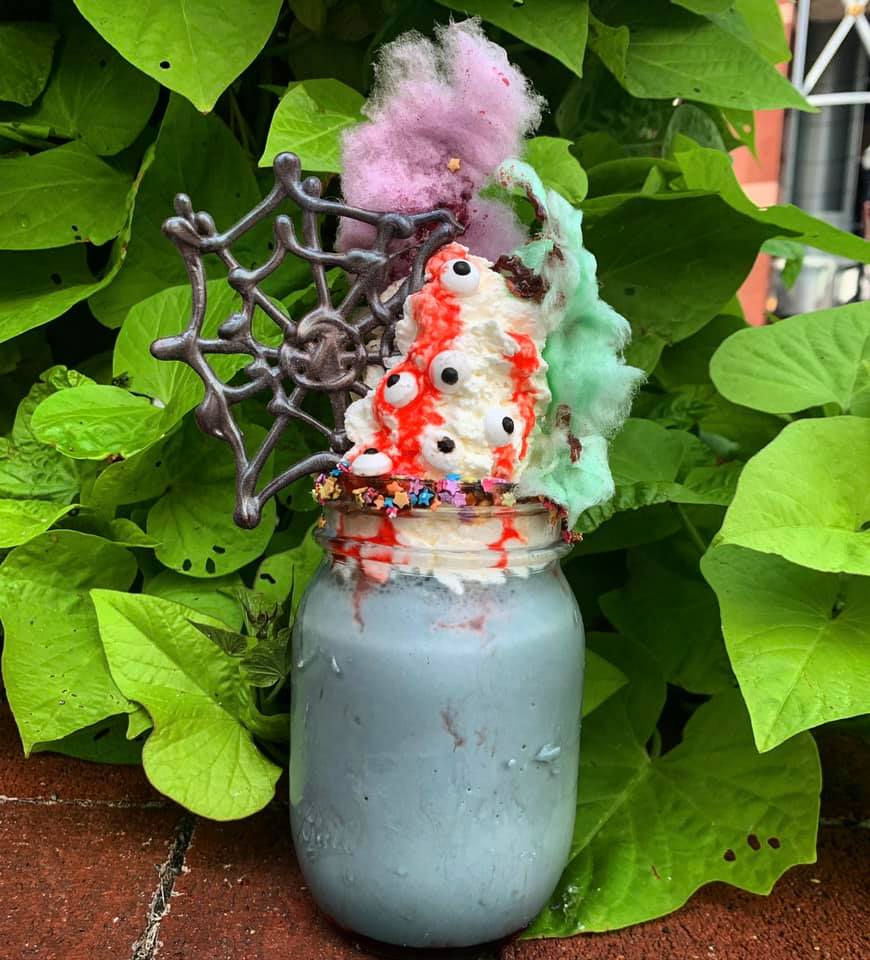 Black ice cream, topped with whipped cream, strawberry sauce, candy eyeballs, cotton candy, chocolate spider web and sprinkle rim.
